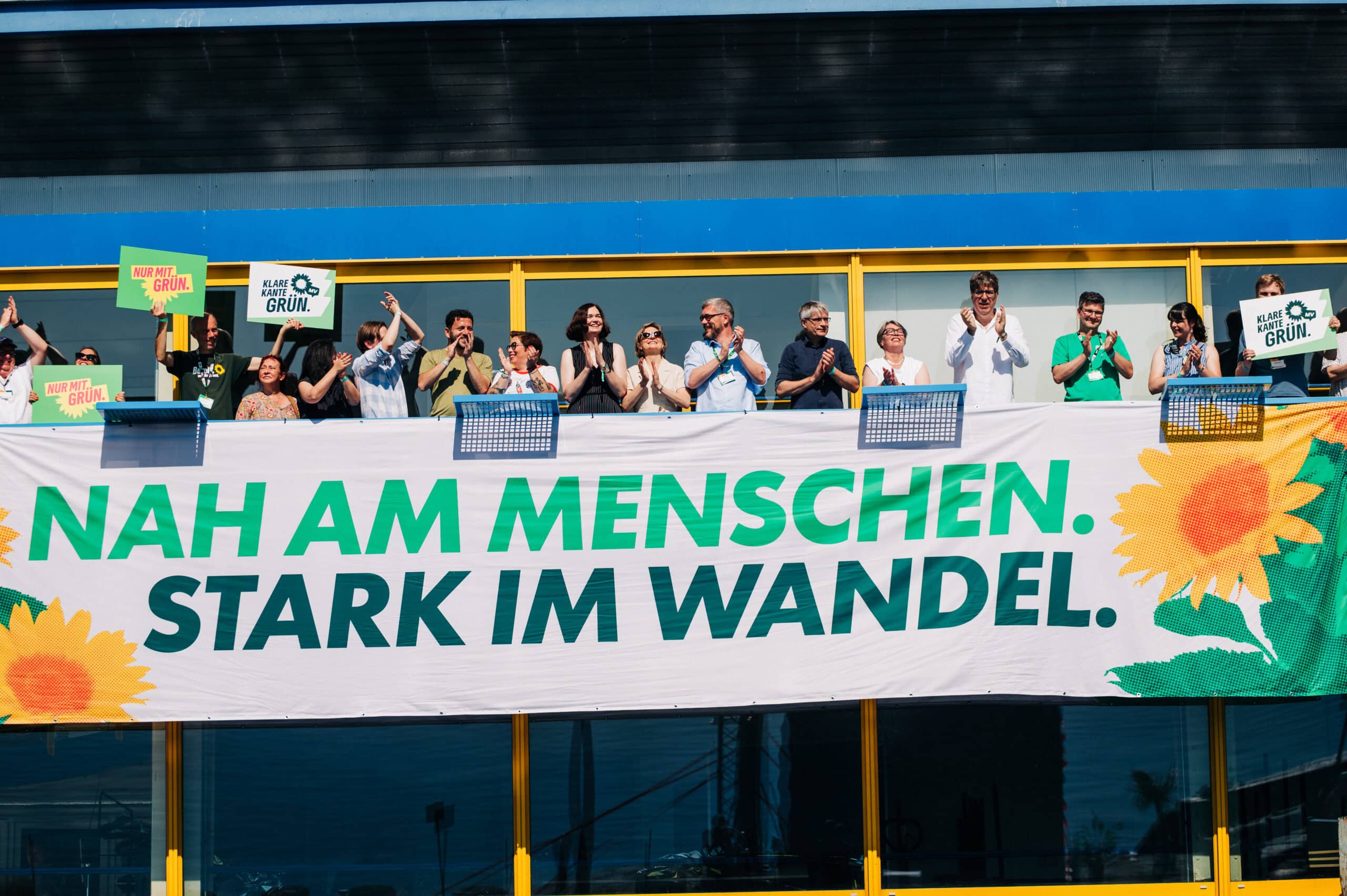 Menschen jubeln hinter einem Banner mit der Aufschrift "Nah am Menschen, stark im Wandel"