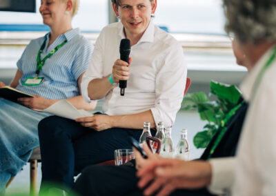 Heiko Knopf sitzt auf einem Podium und spricht in ein Handmikrofon.